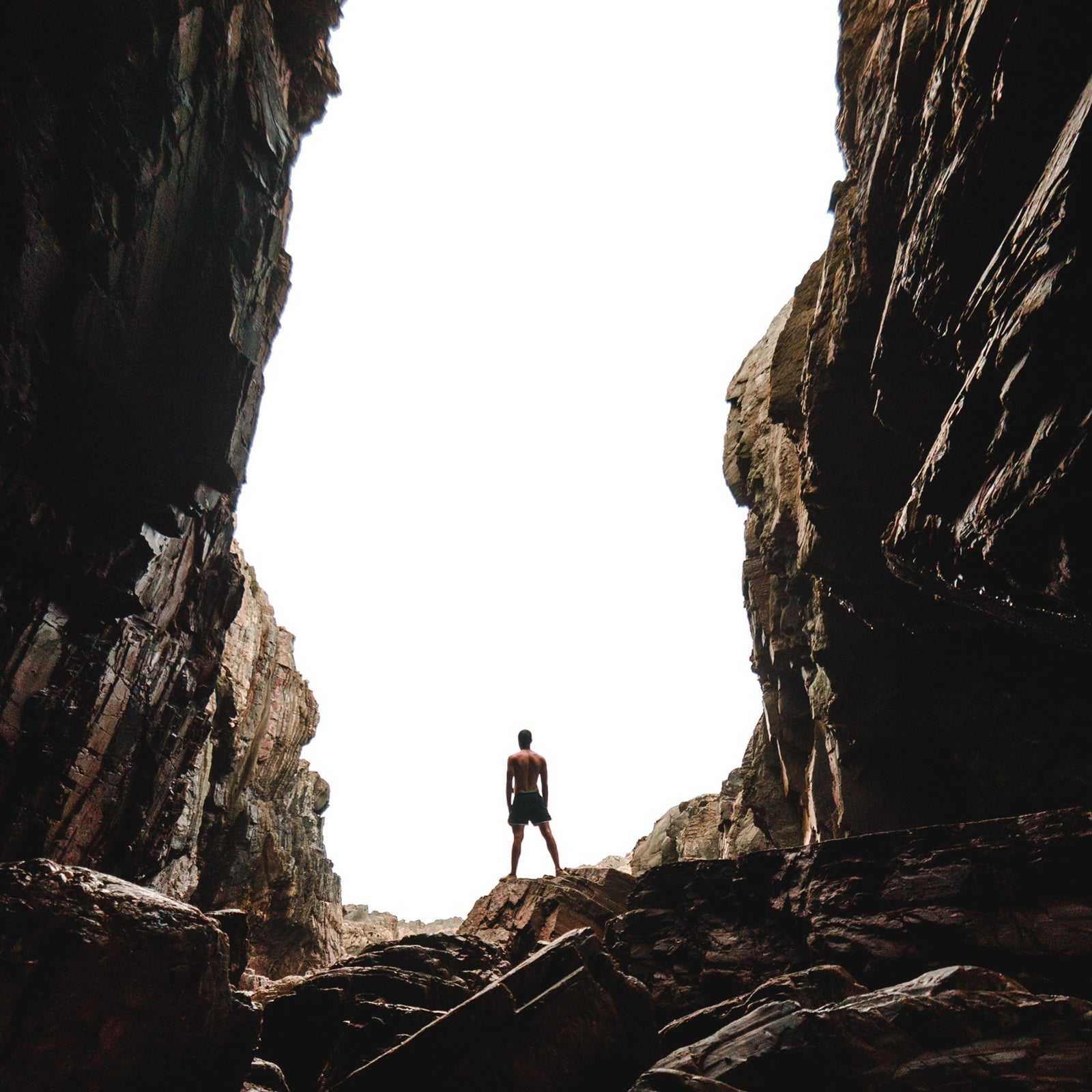 Person standing between coastal cliffs inside a sea cave, evoking exploration and solitude