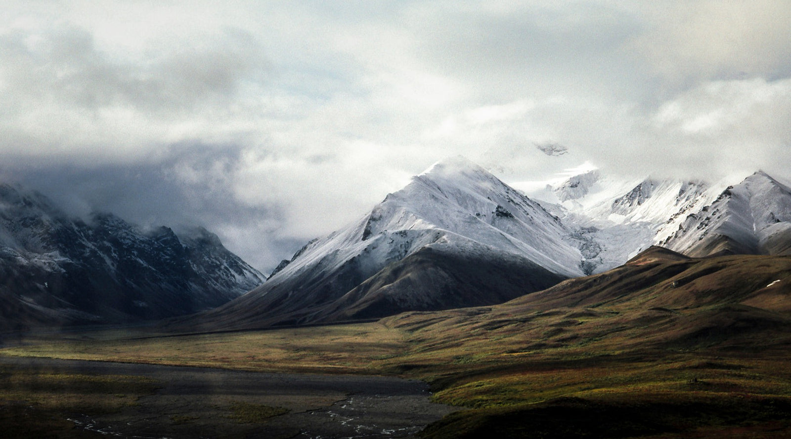 Snow-capped mountain range rising above an open alpine valley under low clouds